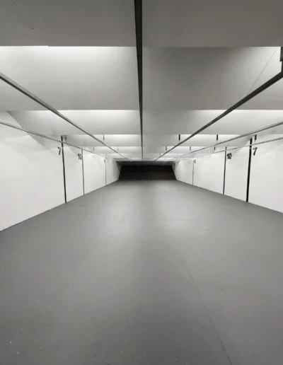 A long, brightly lit indoor shooting range lane viewed from the firing line toward the backstop.